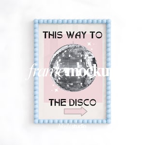 May include: A rectangular wall art print in a light blue beaded frame. The print features a silver disco ball centered on a pale pink background with the black text THIS WAY TO THE DISCO and a pink arrow pointing right at the bottom.