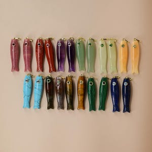 May include: A collection of twenty-two fish-shaped pendants carved from various colourful stones, including red, purple, green, blue, and brown varieties. Each pendant features a small gold-tone metal bail at the top and a single inset gemstone eye.