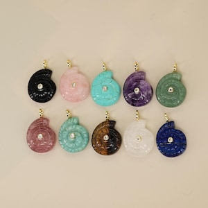 May include: A collection of ten gemstone pendants in a spiral seashell design. The pendants are in various colors, including black, pink, turquoise, purple, and green. Each pendant has a gold-colored bail and a small, round, clear stone in the center.