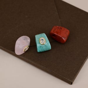 Pu&ograve; includere: Tre perline in pietra con fori. Una &egrave; una perla in quarzo rosa pallido e liscio con un accento in cristallo trasparente bordato d'oro. La perla centrale &egrave; una pietra verde acqua trapezoidale con un cristallo ovale bordato d'oro. La terza &egrave; rossa scura.
