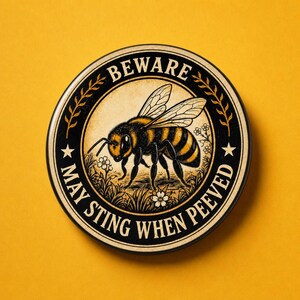 Può includere: Un adesivo circolare con un'illustrazione centrale di un'ape circondata da piccoli fiori. Il design include un bordo nero con il testo BEWARE MAY STING WHEN PEEVED in grassetto, accentuato da due stelle e steli simili a spighe di grano.