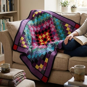 Pode incluir: Uma manta de crochê colorida, feita à mão, com um padrão xadrez em tons de vermelho, amarelo, verde, azul e roxo. A manta está sobre um sofá bege. A borda é roxa e mede cerca de 150 cm x 150 cm.