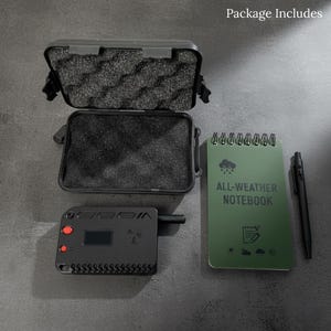 May include: An open black case with foam padding, a black electronic device with red buttons and a small screen, a green spiral-bound notebook with "ALL-WEATHER NOTEBOOK" text, and a black pen. The items are arranged on a dark gray surface.