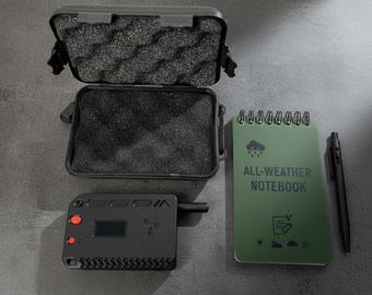 May include: A black, open, protective case with foam, a black electronic device with red buttons and a small screen, a green spiral-bound notebook with "ALL-WEATHER NOTEBOOK" text, and a black pen. Items are on a dark grey surface.