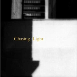 May include: Black and white photograph with the text "Chasing Light" and "Michael Alan" in gold. The image is divided into contrasting areas of light and shadow, with architectural elements visible in the background.