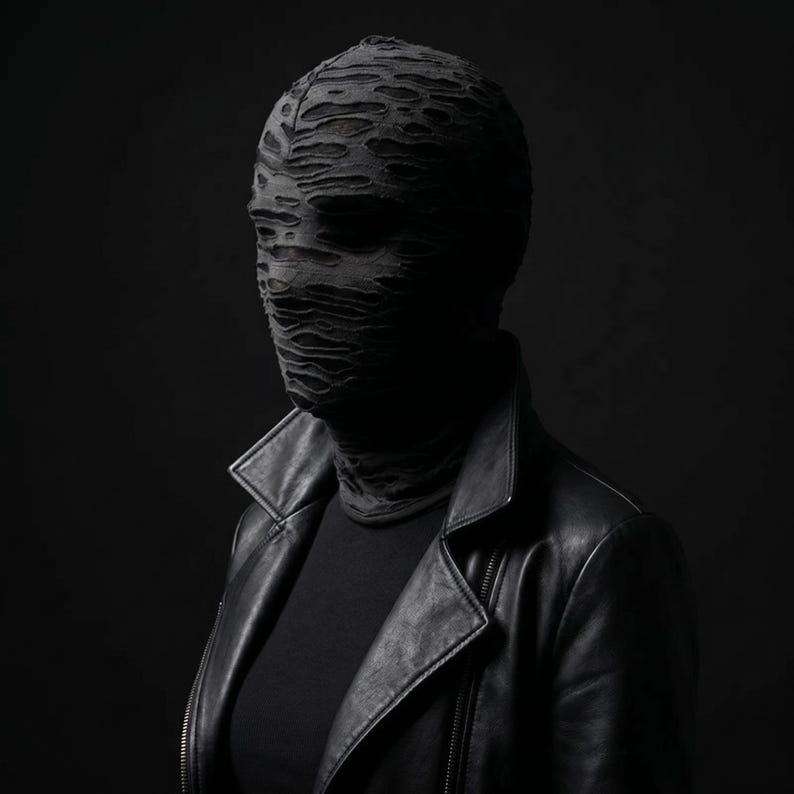 May include: A person wearing a black leather jacket and a distressed fabric mask. The mask covers the entire head and face, with visible tears and openings. The jacket has a classic biker style with a notched collar and zipper closure. The background is a solid black.