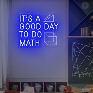 Op de afbeelding: Blauw neonbord met de tekst "IT'S A GOOD DAY TO DO MATH" en wiskundige symbolen. Het bord hangt aan een witte muur. De kamer heeft tafels, stoelen en een schoolbord met wiskundige diagrammen.