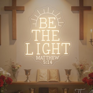 Könnte beinhalten: Ein Neonschild mit dem Text "BE THE LIGHT" und "MATTHÄUS 5:14" in einer Kirche. Das Schild ist von Kreuzen, Blumen, Kelchen und religiösen Statuen umgeben. Das Schild hat eine warme, cremefarbene Farbe.