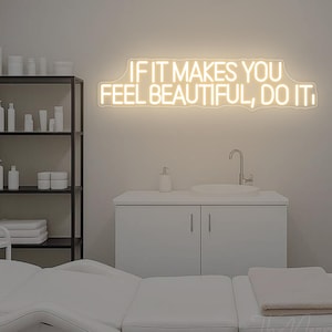 Op de afbeelding: Een schoonheidssalon interieur met een witte behandelbank, planken met producten en een neonreclame met de tekst "IF IT MAKES YOU FEEL BEAUTIFUL, DO IT." De kamer heeft een minimalistische uitstraling met witte muren en meubels.