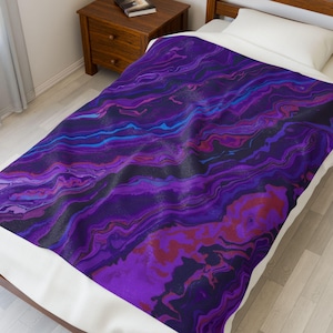 May include: A plush blanket with a vibrant, abstract design. The blanket features flowing patterns in shades of purple, blue, and red, creating a marbled effect. The blanket is displayed on a bed with a white pillow.