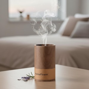 Może przedstawiać: Drewniany dyfuzor olejków eterycznych z napisem "HomeFlower" na brązowej etykiecie. Para unosi się z góry. Gałązka lawendy i ciemne nasiona leżą na stole. Dyfuzor jest cylindryczny.