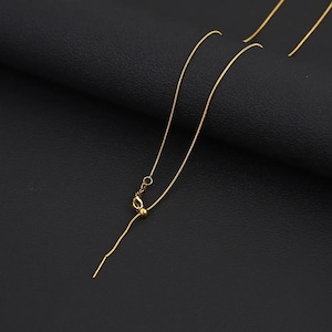 May include: A thin gold-tone snake chain necklace featuring an adjustable sliding bead mechanism. The chain is delicate and flexible, with a small metal clasp and a smooth, polished finish that reflects light along its slender, continuous length.