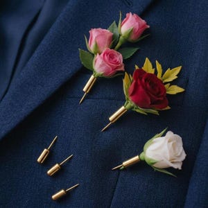 May include: A navy blue suit jacket adorned with several floral boutonnieres. The boutonnieres feature pink, red, and white roses with gold-colored pin stems. Several loose gold pins are also visible.