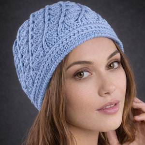 Könnte beinhalten: Hellblaue Strickmütze mit strukturiertem Zopfmuster. Die Mütze ist aus weichem Garn gefertigt und hat einen gerippten Saum. Die Mütze wird von einer Person getragen.