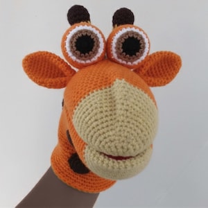 Könnte beinhalten: Handgefertigte orangefarbene und beige Häkel-Giraffenpuppe mit großen, ausdrucksstarken Augen, braunen Flecken und kleinen Ohren. Die Puppe ist so konzipiert, dass sie über eine Hand passt.