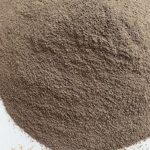May include: A close-up shot of a pile of finely ground, dark brown powder, likely a spice or seasoning, on a white plate. The powder has a granular texture and forms a small mound.