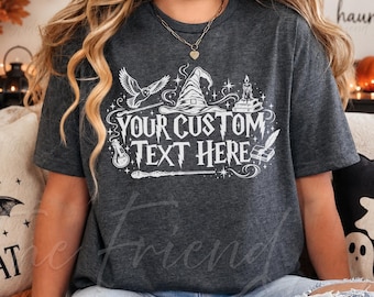May include: A dark heather gray short-sleeve t-shirt featuring a white graphic print of a wizard hat, an owl, a candle, a potion bottle, and a wand. The text "YOUR CUSTOM TEXT HERE" is printed in the center in a stylized, magical-themed font.