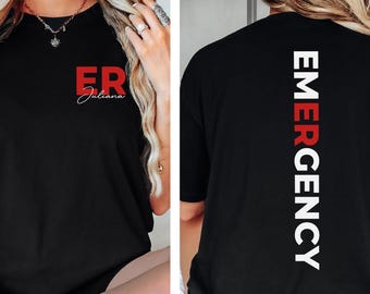 May include: A black t-shirt featuring a red ER logo with the name Juliana in white script on the front left chest. The back of the shirt displays the word EMERGENCY printed vertically in large white letters with the letters EMER in red.