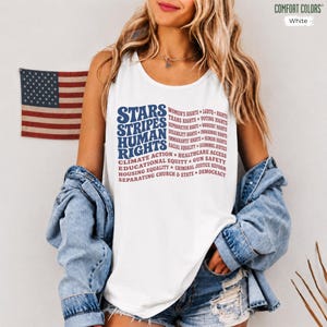 May include: A white sleeveless tank top featuring blue and red text that reads Stars Stripes Human Rights, followed by a list of social causes including Women's Rights, LGBTQ Rights, Voting Rights, Climate Action, and Healthcare Access.