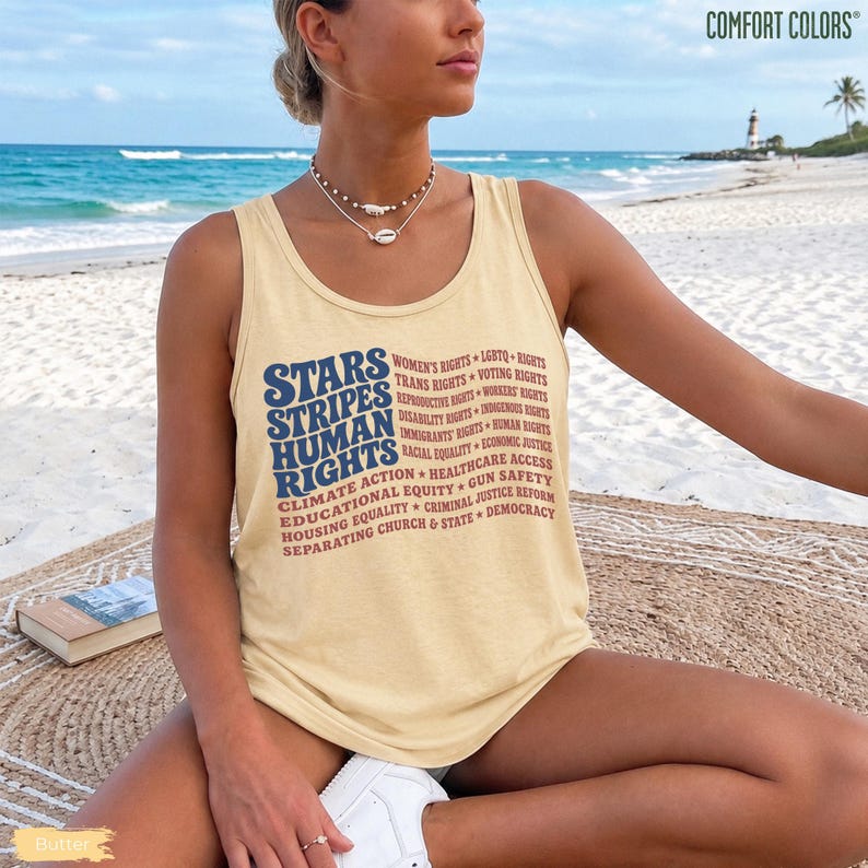 May include: A light yellow tank top featuring the text STARS STRIPES HUMAN RIGHTS in blue, followed by a list of social causes in red, including Women's Rights, LGBTQ Rights, Trans Rights, Voting Rights, Reproductive Rights, Workers' Rights, and Democracy.