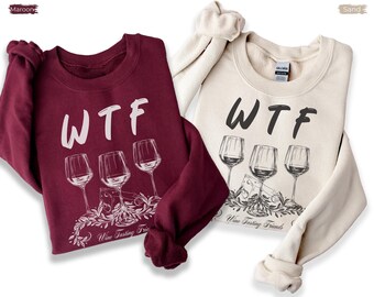 May include: Two crewneck sweatshirts in maroon and sand colors. Each features the text "WTF" above a graphic of three wine glasses, a wedge of cheese, and leafy vines. The text "Wine Tasting Friends" is printed below the graphic illustration.