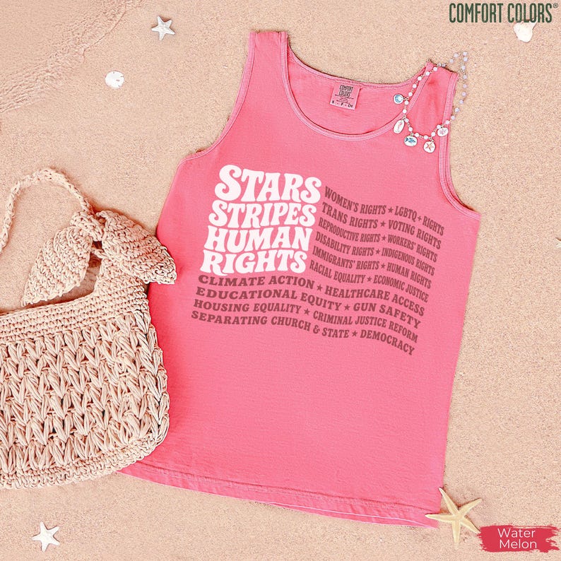May include: A coral pink sleeveless tank top featuring white text that reads STARS STRIPES HUMAN RIGHTS followed by a list of social causes including Women's Rights, LGBTQ+ Rights, Trans Rights, Voting Rights, and Racial Equality.