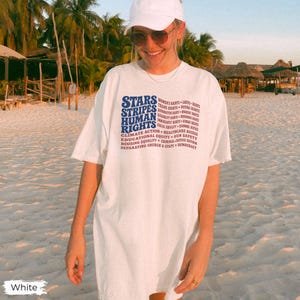 May include: A white short-sleeve t-shirt featuring blue and red text that reads STARS STRIPES HUMAN RIGHTS followed by a list of social causes including Women's Rights, LGBTQ+ Rights, Trans Rights, Voting Rights, Reproductive Rights, and Workers' Rights.
