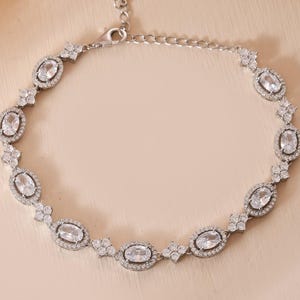 Könnte beinhalten: Ein silberfarbenes Armband mit ovalen, klaren Edelsteinen. Das Armband hat ein zartes Design mit kleineren, runden Edelsteinen zwischen den Ovalen. Der Verschluss ist im Hummerkrallen-Stil.