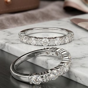 Könnte beinhalten: Zwei silberne Ringe mit mehreren runden Diamanten. Die Ringe liegen auf einer weiß-grauen Marmoroberfläche. Einer der Ringe ist fokussiert und zeigt die Punzierung '925'.
