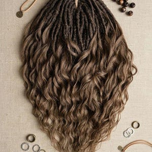 Könnte beinhalten: Ein Set aus braunen synthetischen Haarverlängerungen mit dunkelbraunen Dreadlocks am Ansatz, die in lockeres, welliges hellbraunes Haar in den Spitzen übergehen. Das Set enthält mehrere kleine Metallringe für das Haar sowie Holzperlen.