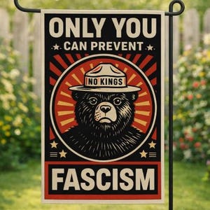 May include: A garden flag with a black metal pole. The flag features a bear wearing a ranger hat inside a red and yellow circle. Text on the flag reads "ONLY YOU CAN PREVENT FASCISM" and "NO KINGS".