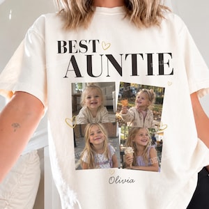 May include: An ivory t-shirt featuring the black text BEST AUNTIE at the top, accompanied by four square photographs of a young child. Below the photos, the name Olivia is printed in black script, with small gold heart outlines scattered around.