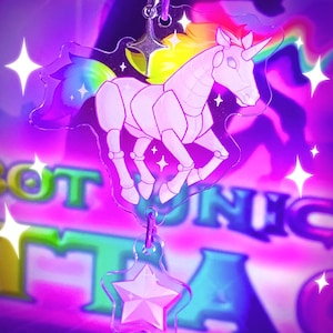May include: A clear acrylic charm featuring a robotic unicorn with a rainbow mane and tail. The charm has a star-shaped pendant and a silver-colored star at the top. The background is a vibrant mix of purple, pink, and green.