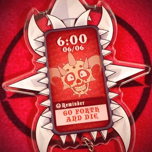 May include: A clear acrylic keychain featuring a red rectangle with a skull illustration and the text "6:00 06/06". The keychain also has the text "Reminder GO FORTH AND DIE" and is surrounded by a white and gray jagged design.