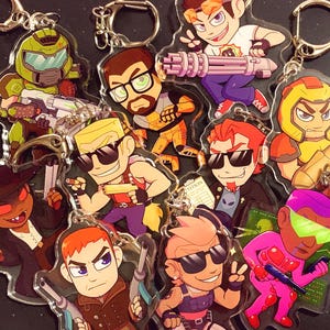 May include: A selection of clear acrylic keyrings featuring cartoon characters in action poses. The keyrings display characters with vibrant colours and detailed designs. Each keyring has a silver-coloured ring attached.