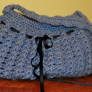 May include: A blue crocheted tote bag with black ribbon ties. The bag has a crocheted handle and a textured design.