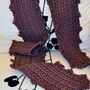 May include: A brown knitted scarf with a scalloped edge. The scarf is folded in half and draped over a white surface with a black floral design.