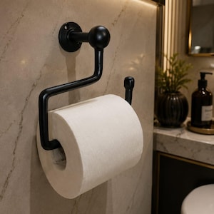 May include: A matte black metal toilet roll holder with a wall-mounted circular base, a curved arm, and a vertical end post. The holder features a spherical finial at the top and holds a standard roll of white toilet paper in a horizontal position.