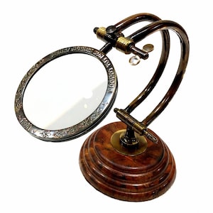 May include: A vintage magnifying glass with a dark brown wooden base and a curved brass frame. The magnifying glass has a decorative silver rim with the text "HENRY HUGHES & SON LTD. LONDON" and the year "1941".