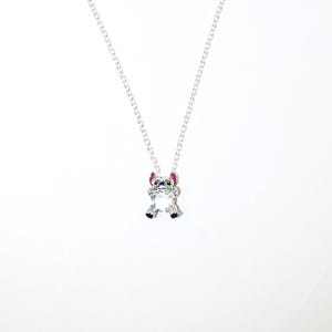 Op de afbeelding: Een zilveren ketting met een hanger van het personage Stitch. De hanger is een heldere, facetgeslepen kristal met blauwe, roze en zwarte details. De ketting is een fijne zilveren schakelketting.