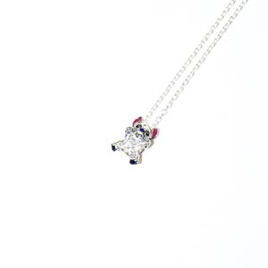 Op de afbeelding: Een zilveren ketting met een hanger die een stripfiguur voorstelt. De hanger heeft een groot, vierkant, helder kristallen lichaam, met blauwe, roze en zilveren details. De ketting is ook zilver.