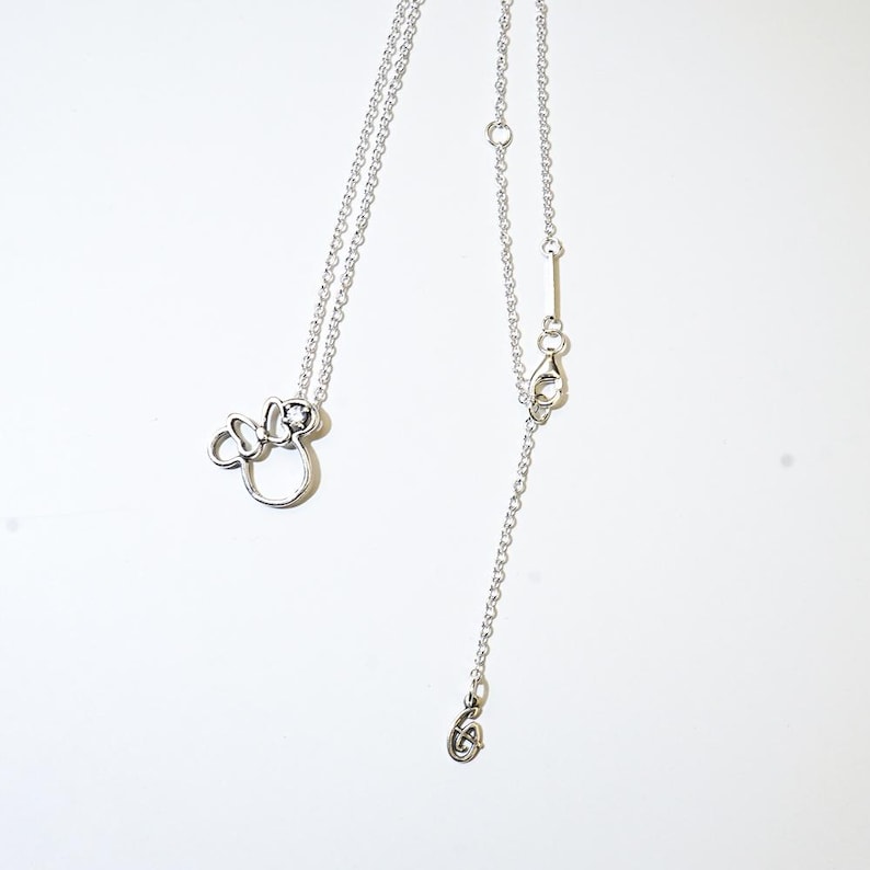 Puede incluir: Un collar plateado con un colgante de lazo de Minnie Mouse. El collar tiene una cadena fina con una longitud ajustable y un cierre de mosquet&oacute;n. El colgante es un contorno estilizado del ic&oacute;nico lazo de Minnie Mouse.