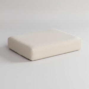 Peut inclure: Un coussin rectangulaire blanc cassé aux coins arrondis. Le coussin a une texture côtelée et est posé sur un fond blanc uni. La couleur neutre et le design simple suggèrent un accent sur le confort et l'esthétique minimaliste.