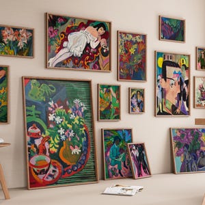 May include: A collection of framed abstract paintings in various sizes and styles, displayed on a neutral wall. The artwork features vibrant colors, floral and figurative subjects, and a range of artistic techniques. Wooden stools and a table are in the foreground.