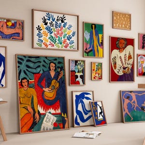 Peut inclure: Une collection d'impressions d'art encadrées de différentes tailles et styles, exposées sur un mur neutre. Les œuvres présentent des figures abstraites, des motifs floraux et des portraits aux couleurs vives. Des tabourets en bois et une table sont au premier plan.