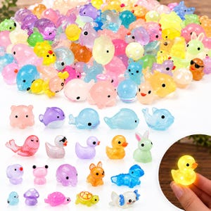 May include: A large collection of miniature animal figurines made of translucent, colorful resin. The assortment includes tiny ducks, whales, rabbits, frogs, and turtles in various bright hues. One yellow duck is shown glowing in the dark.