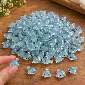 May include: A large pile of small, translucent, light blue seal-shaped resin cabochons. Each seal features a smooth, rounded body with tiny black dots for eyes and a nose, creating a uniform appearance across the collection of miniature figures.