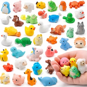 May include: A selection of small, brightly coloured animal figurines, such as a penguin, sheep, duck, frog, and crab. The figurines are made of a smooth material and come in various colours including pink, yellow, green, and blue. Some are held in a hand.