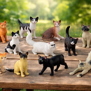 May include: A collection of eleven small cat figurines in various poses and colors, including orange, black, white, brown, and Siamese patterns, arranged on a weathered wooden surface. The figures display diverse markings and textures.