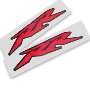 Könnte beinhalten: Zwei rot-schwarze RX-Logo-Aufkleber auf weißem Hintergrund. Die Aufkleber haben ein stilisiertes Design mit scharfen Winkeln und einer fetten Schriftart. Die Aufkleber sind wahrscheinlich für ein Motorrad oder ein Fahrzeug.